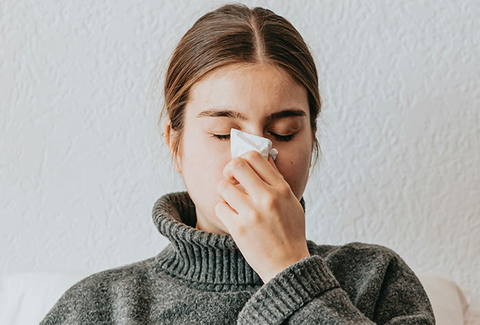Person with gray sweater using tissue, related to worst plane seatmates.