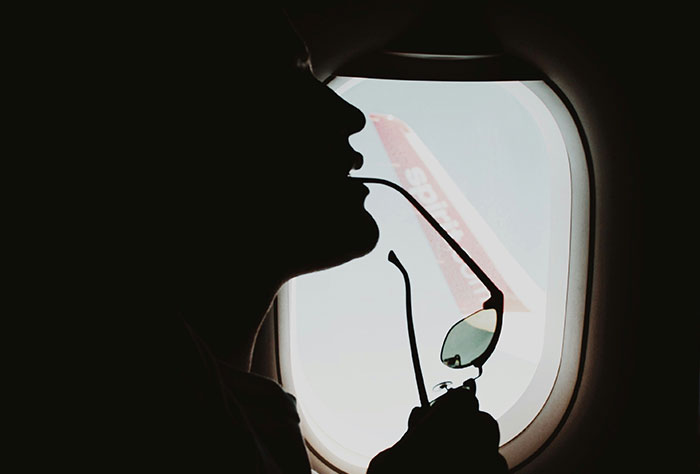Silhouette of a plane passenger holding sunglasses near an airplane window, illustrating uncomfortable seatmates.
