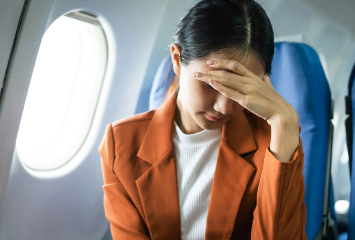 Person seated on a plane, appearing frustrated, covering face with hand.
