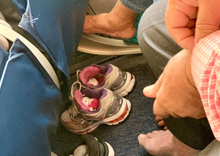 Barefoot passengers with shoes off in a cramped airplane seating area, illustrating uncomfortable plane seatmates.
