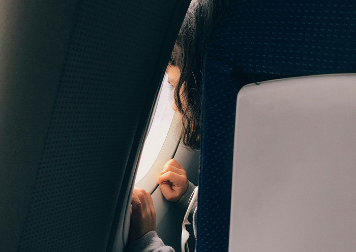 Child peering out of a plane window, illustrating worst seatmates on a flight.