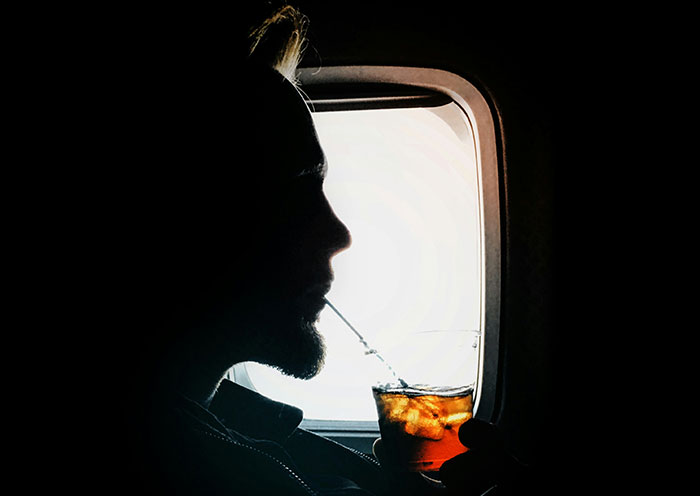Silhouette of a plane seatmate sipping a drink by a window.