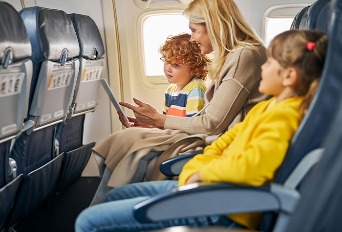 Woman and two kids seated on a plane, sharing a tablet.
