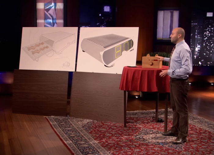 Man presenting a product prototype on Shark Tank stage with design boards, illustrating Shark Tank products that flopped.