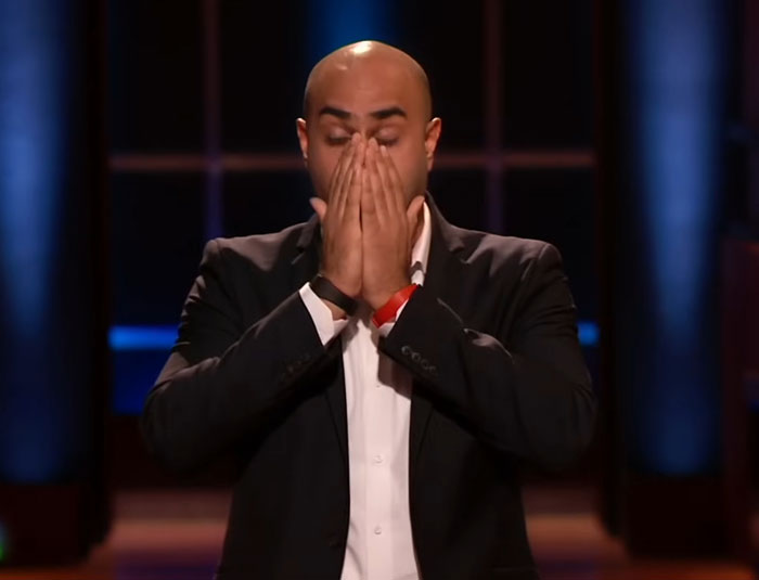 Man covering face with hands on Shark Tank set, expressing disappointment over failed Shark Tank products.