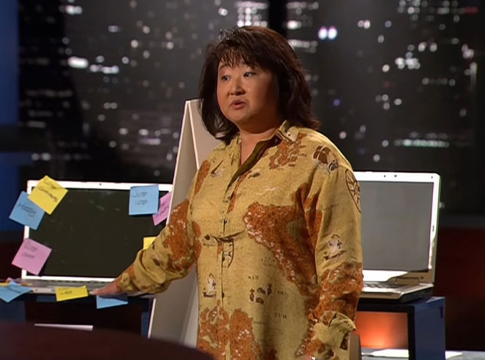 Woman presenting a product on Shark Tank stage with laptops covered in sticky notes, related to Shark Tank products flop.