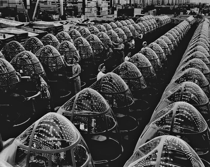 Women assembling aircraft canopies in WWII factory, rows of transparent domes reflecting light, showcasing wartime production.