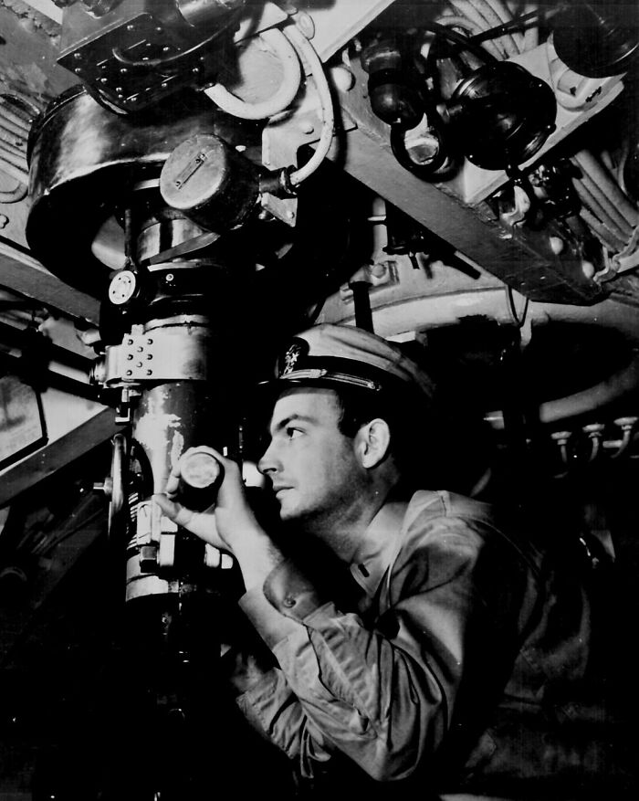 Soldier using a periscope in a WWII submarine, focusing intently on the equipment around him.