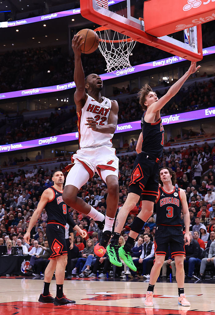 Basketball player in a white uniform making a jump shot against opponents in a crowded stadium.