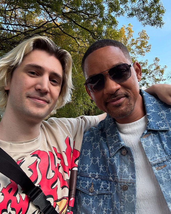 Two individuals including streamer xQc posing outdoors; one wearing a patterned shirt, the other in denim and sunglasses, discussing net worth.