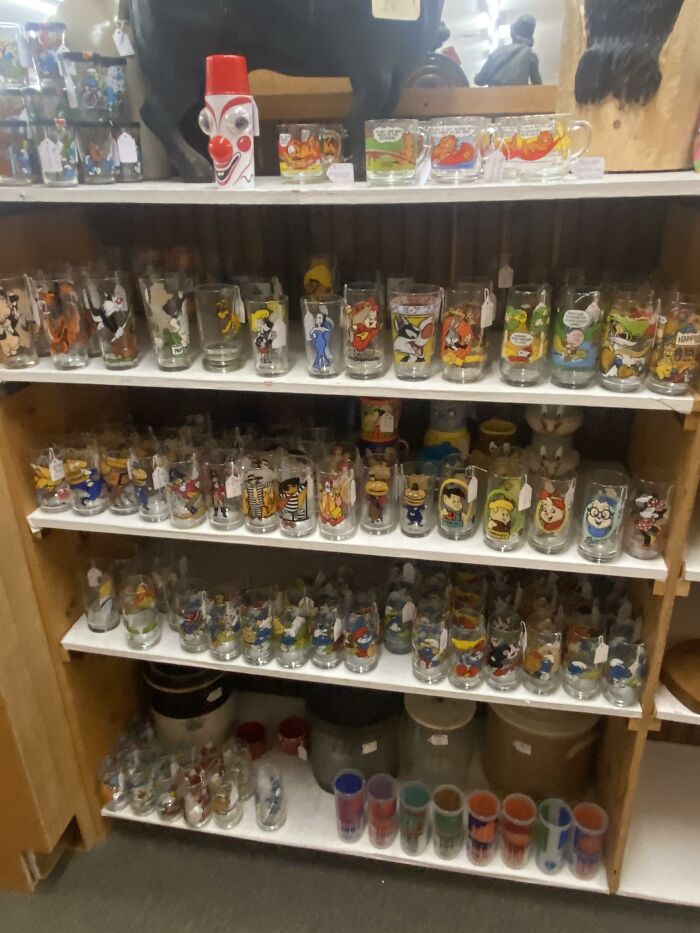 Collection of vintage glassware with cartoon characters displayed on wooden shelves in an organized manner.