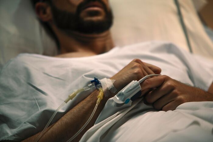 A man lying in a hospital bed, with IV lines attached, looking contemplative.