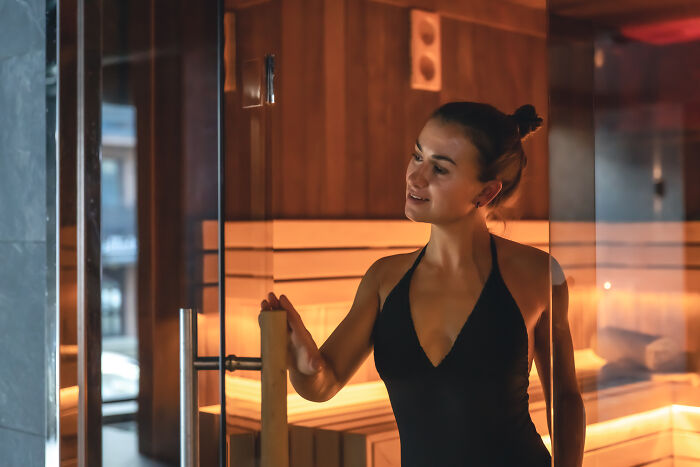 Woman in a swimsuit entering a modern wooden sauna, exemplifying European wellness culture.