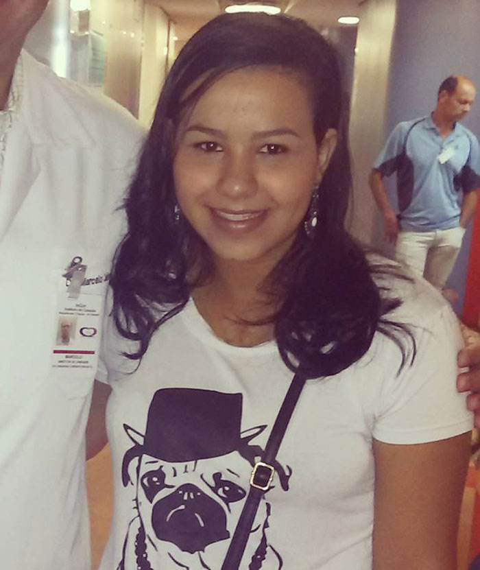 A woman in a white shirt with a pug design, smiling in a hospital corridor. A woman in a white shirt with a pug design, smiling in a hospital corridor.