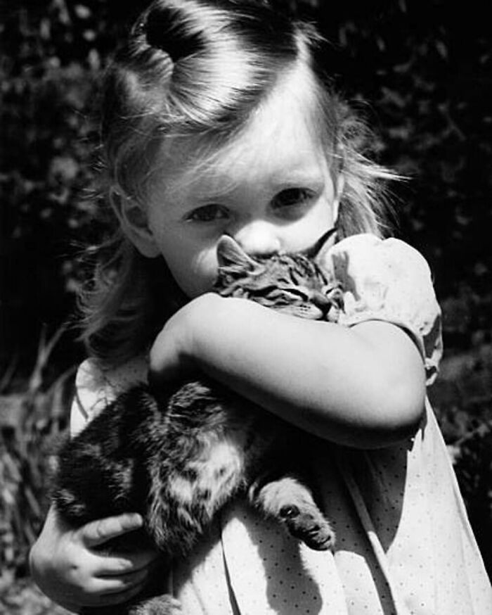 Vintage black and white photo of a young girl lovingly holding and hugging a tabby cat outdoors.