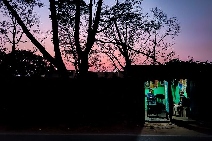 Two people sitting inside a small lit room at dusk with bare trees outside, capturing Simultala's timeless escape vibe.