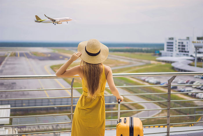 Woman in yellow dress with suitcase at airport, watching plane take off, reflecting on solo holiday and friend invitation situation Woman in yellow dress with suitcase at airport, watching plane take off, reflecting on solo holiday and friend invitation situation