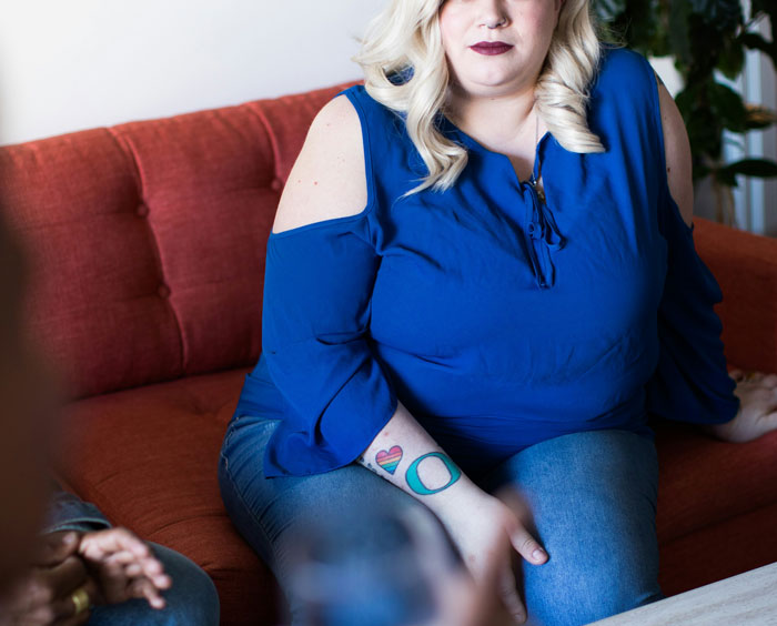 Obese woman in blue top sitting on a couch during a conversation about newborn babysitting and fat shaming.