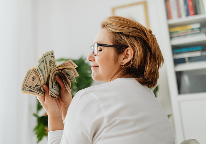 Woman holding cash with a satisfied expression, representing life insurance policy and car refinancing issues. Woman holding cash with a satisfied expression, representing life insurance policy and car refinancing issues.