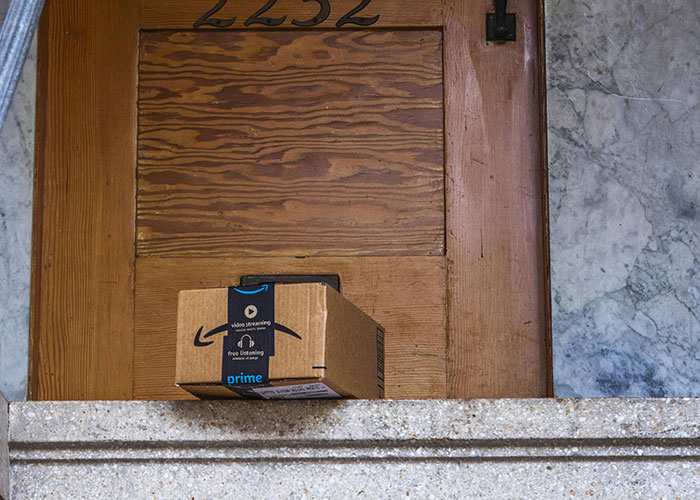 Amazon package left on doorstep outside wooden door, illustrating package stealing and petty neighbor actions.