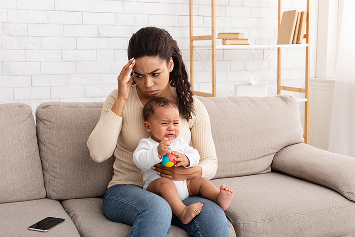 Woman looking stressed while holding crying baby, illustrating conflict over babysitting payment with sister.