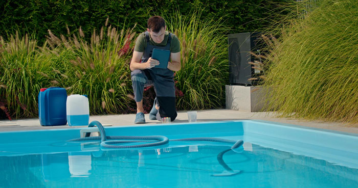 Man inspecting pool equipment with tablet beside a residential pool amid neighbors sending relatives without consent
