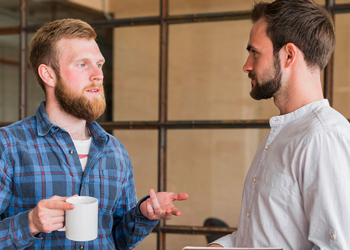 Two male employees in casual office setting having a serious discussion about employee suit and boss demotion.