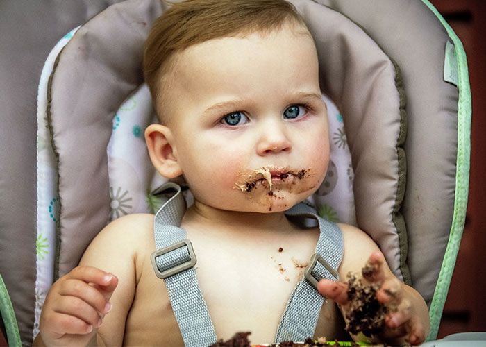 Toddler with cake smudged on face and hands sitting in high chair after cake was moved away from destroying it. Toddler with cake smudged on face and hands sitting in high chair after cake was moved away from destroying it.