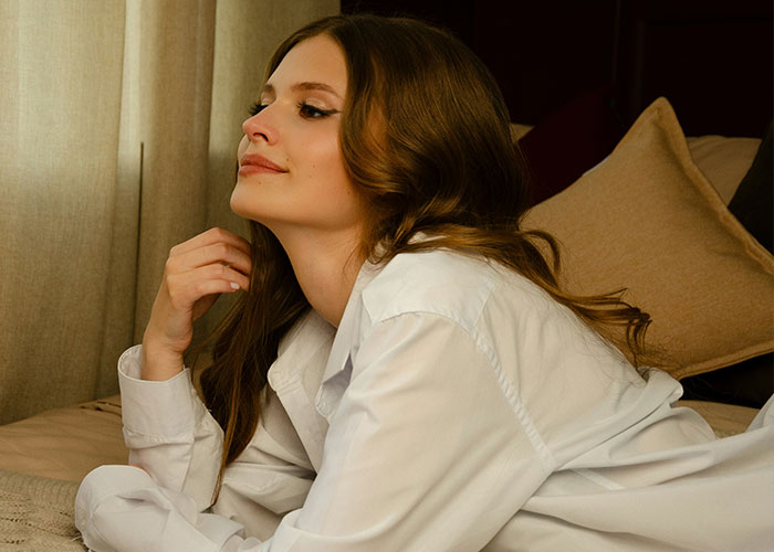 Woman in a white shirt looking thoughtful, reflecting on an emotional moment with her husband&rsquo;s childhood best friend.