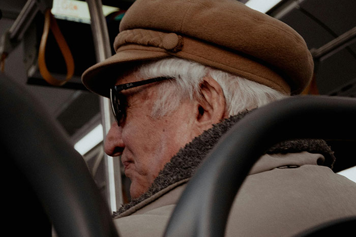 Elderly man wearing a brown hat and sunglasses on a bus, illustrating a small act of kindness for an unexpected conversation.