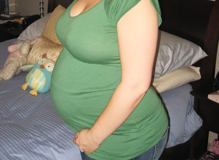 Pregnant woman in green shirt sitting on bed, highlighting issue of recognition as mom and Mother's Day gift refusal.