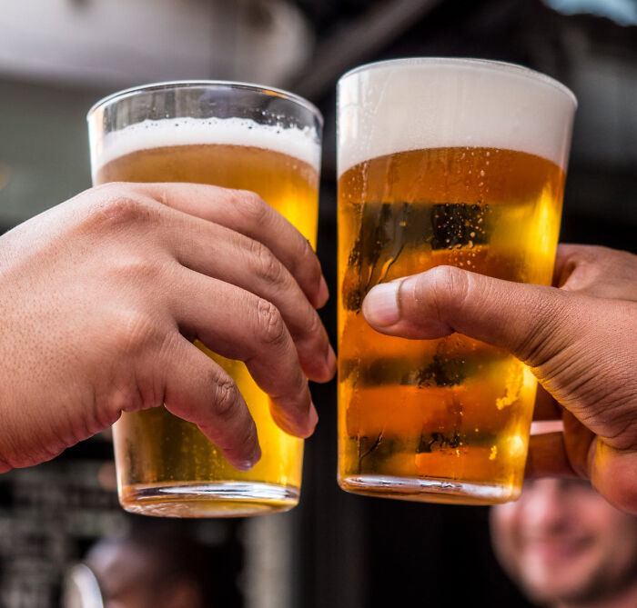 Two hands clinking glasses of beer, illustrating national stereotypes about drinking cultures and humor.