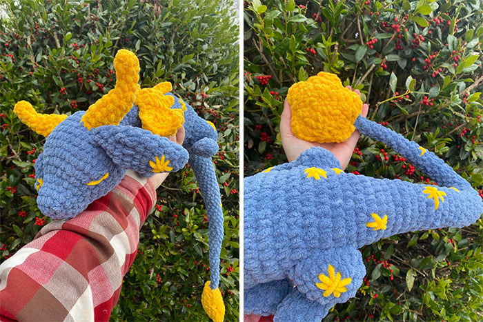 Crochet masterpiece of a blue and yellow dragon held outdoors with detailed crocheted flowers and textures