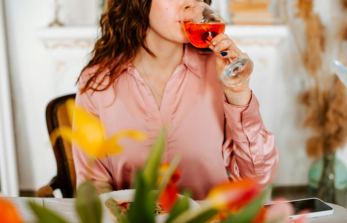 Woman in a pink blouse drinking wine, illustrating problematic behaviors women get a pass for according to men.