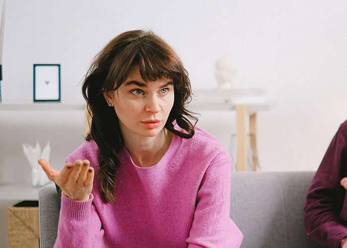 Woman in a pink sweater sharing surprisingly entertaining facts during a casual conversation in a bright living room setting.