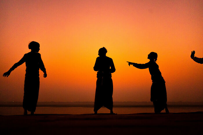 Silhouettes of people interacting during sunset, showcasing compelling street photography moments in a vibrant outdoor setting.