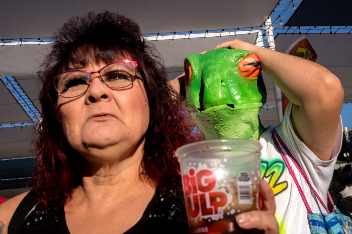 Woman with glasses and person in a frog mask at an outdoor event, capturing unique street photography moments.
