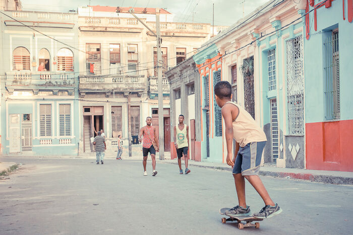 Boy skateboarding on a colorful street with textured buildings and people walking, captured in vibrant street photography moment.