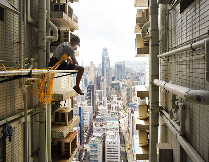 Man sitting on ledge high above city street, showcasing street photography moments captured by talented photographers.