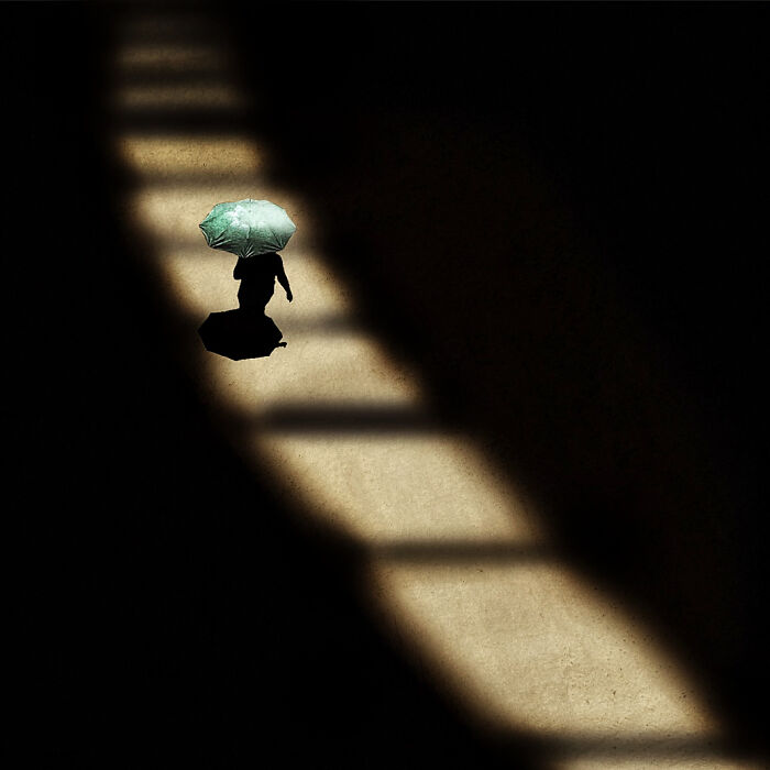 Person walking with a green umbrella casting a shadow on a sunlit path in a striking street photography moment.