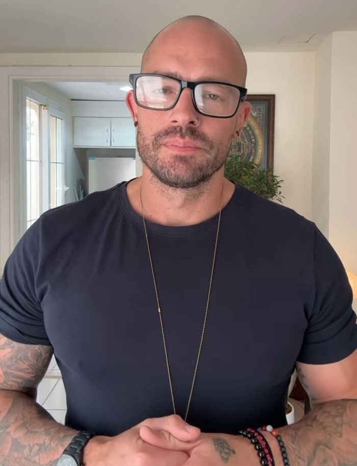 Man with glasses and tattoos standing indoors, former pole dancer turned monk sparking mixed reactions with his story
