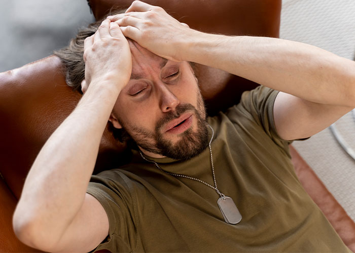 Man in army-green shirt holding his head in pain, illustrating the theme of pathetic injuries shared by 109 people.