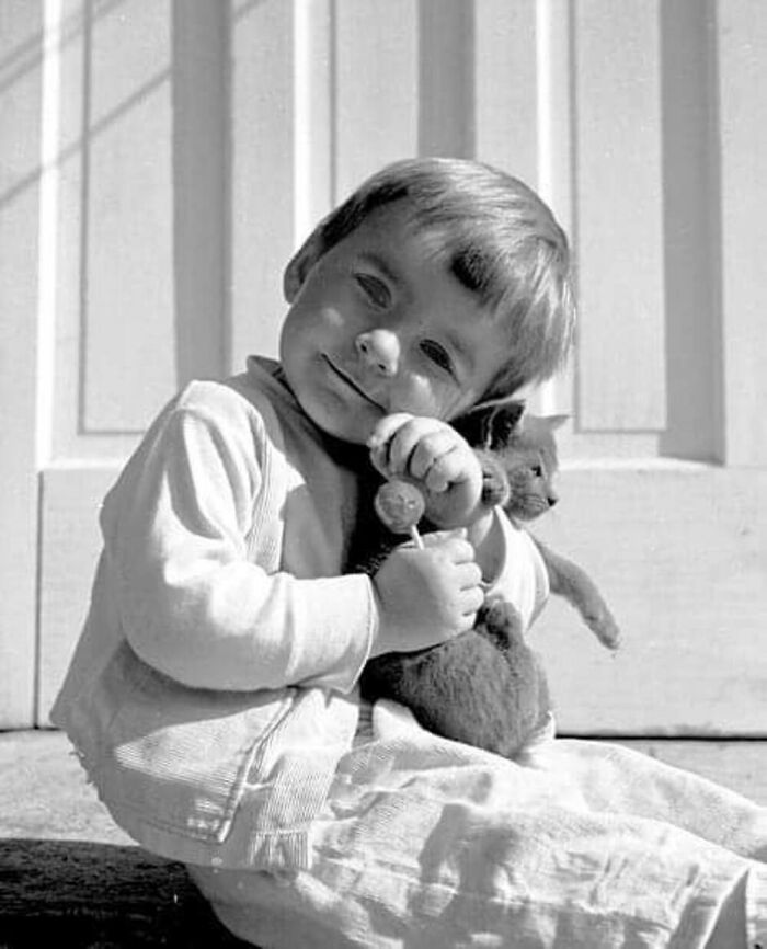 Vintage black and white photo of a young child sitting and hugging a kitten, showcasing the timeless bond between kids and cats.