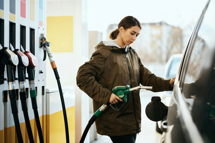 Woman at gas station fueling car, illustrating common ways people lose money while thinking they’re saving.