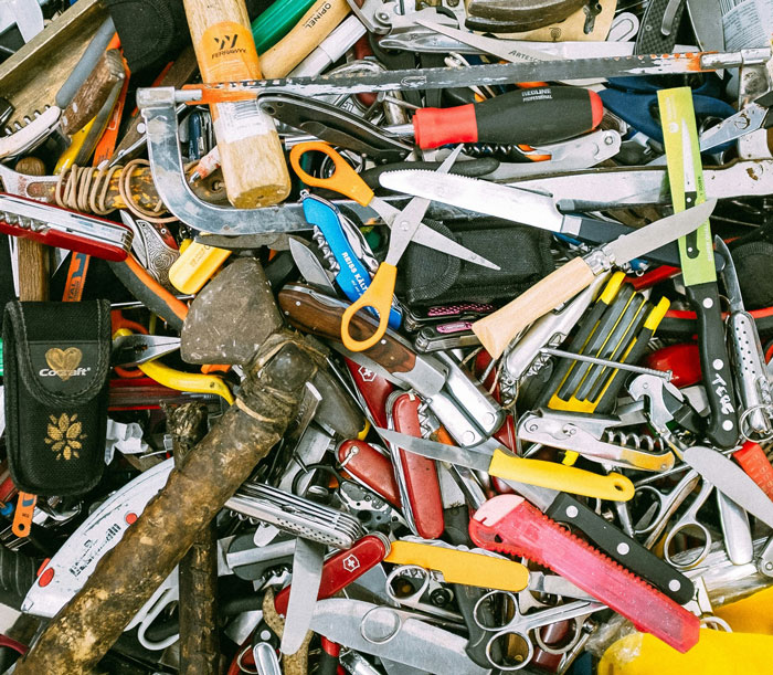 A cluttered collection of assorted hand tools and knives piled together, illustrating a habit of saving and reusing items.