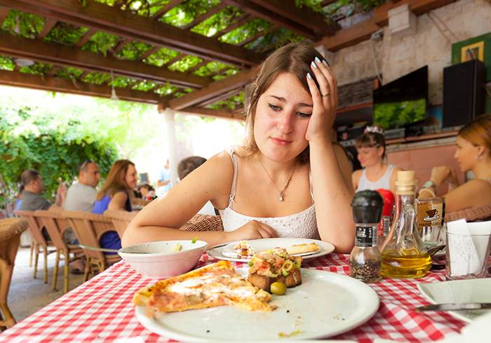 Woman looking sad while eating at a restaurant, excluded from BF’s family vacation due to gluten intolerance. Woman looking sad while eating at a restaurant, excluded from BF’s family vacation due to gluten intolerance.