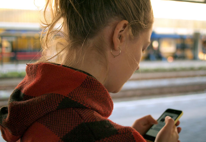 Young woman in a red plaid jacket using smartphone at a train station illustrating problematic behaviors women get a pass for