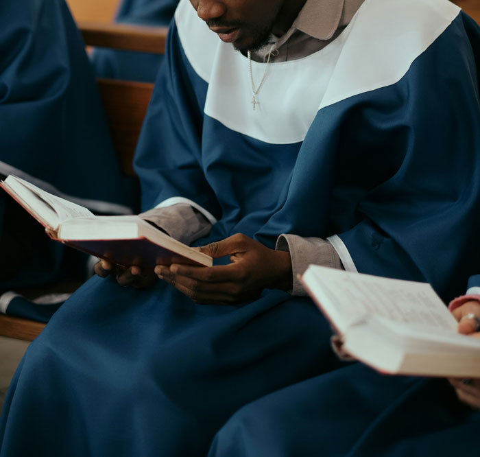 Person in a blue choir robe reading a book, representing stories of people who escaped from cults and sharing experiences.