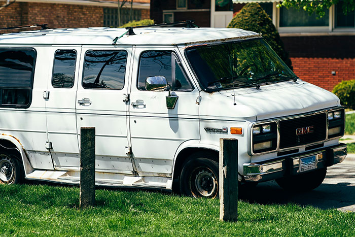 White GMC van with a flat tire parked near a brick building, evoking a scary we need to leave now gut feeling moment.
