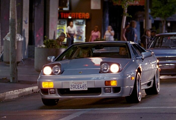 Silver sports car with pop-up headlights driving at night in an urban setting, demonstrating fascinating today I learned facts.